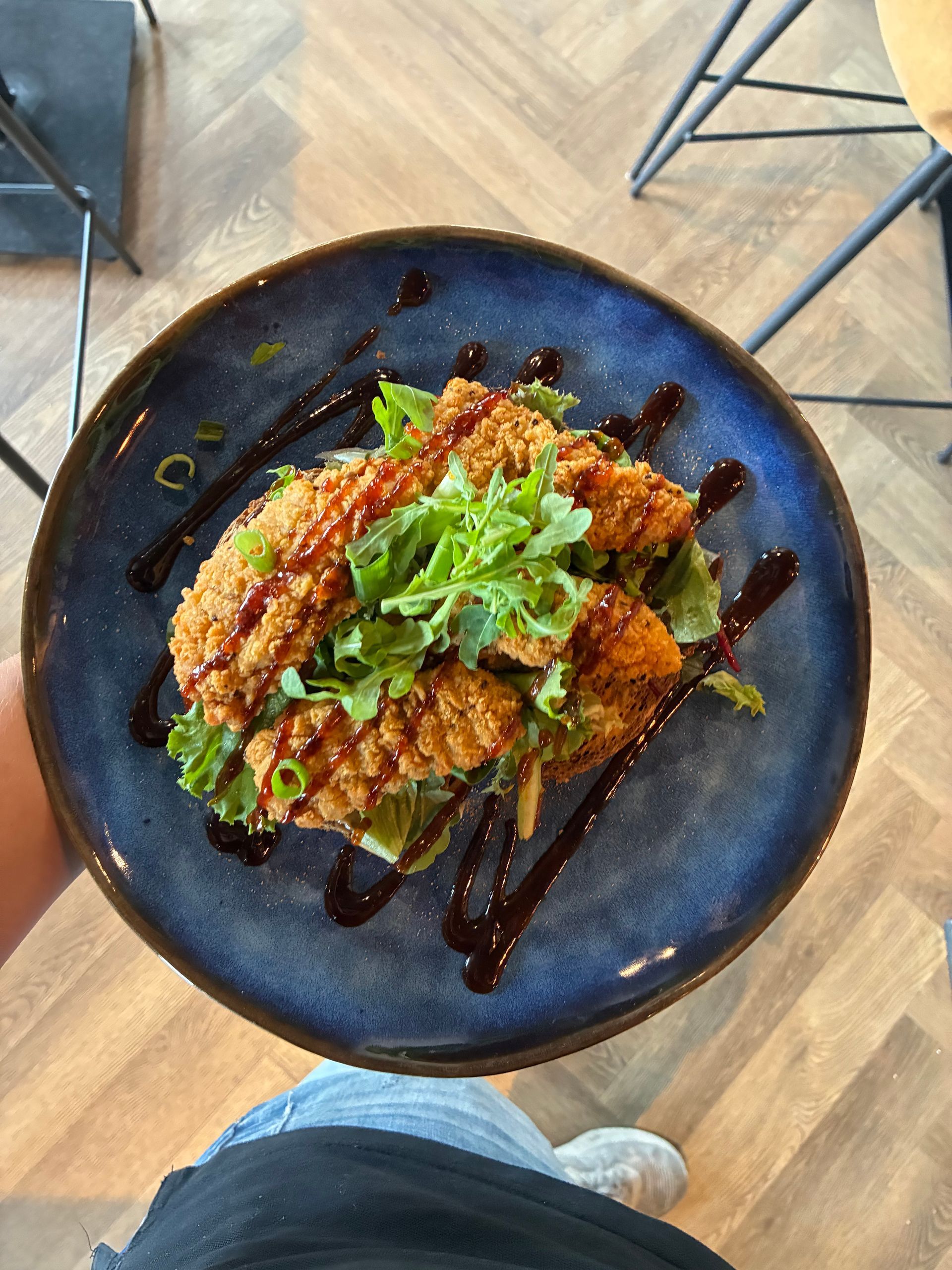 Gebakken kip met groenten en saus op een blauw bord.