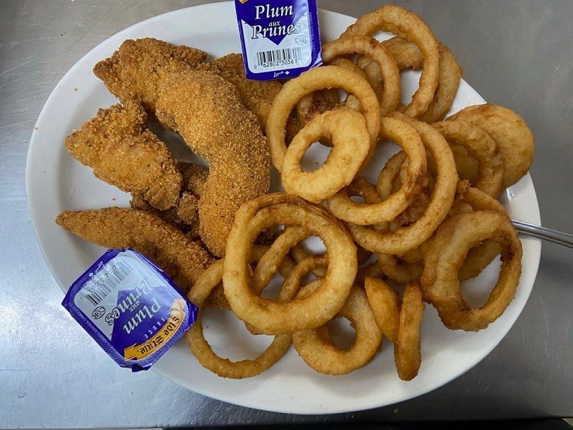 A white plate topped with chicken tenders , onion rings and a bottle of plum sauce.