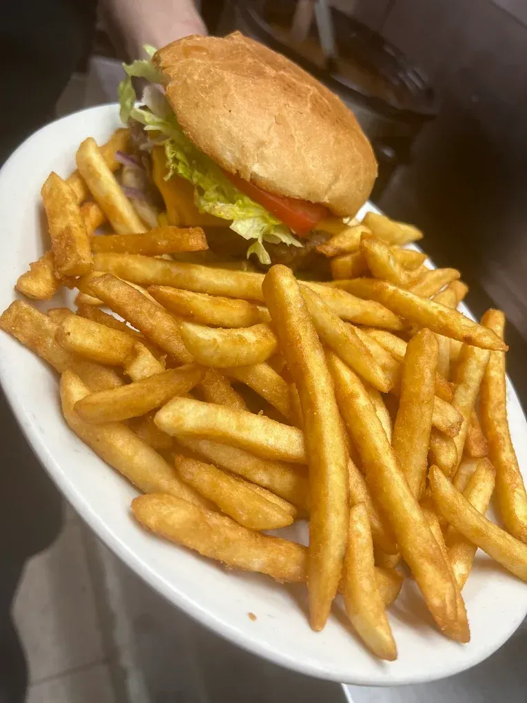 A person is holding a plate of french fries and a hamburger.