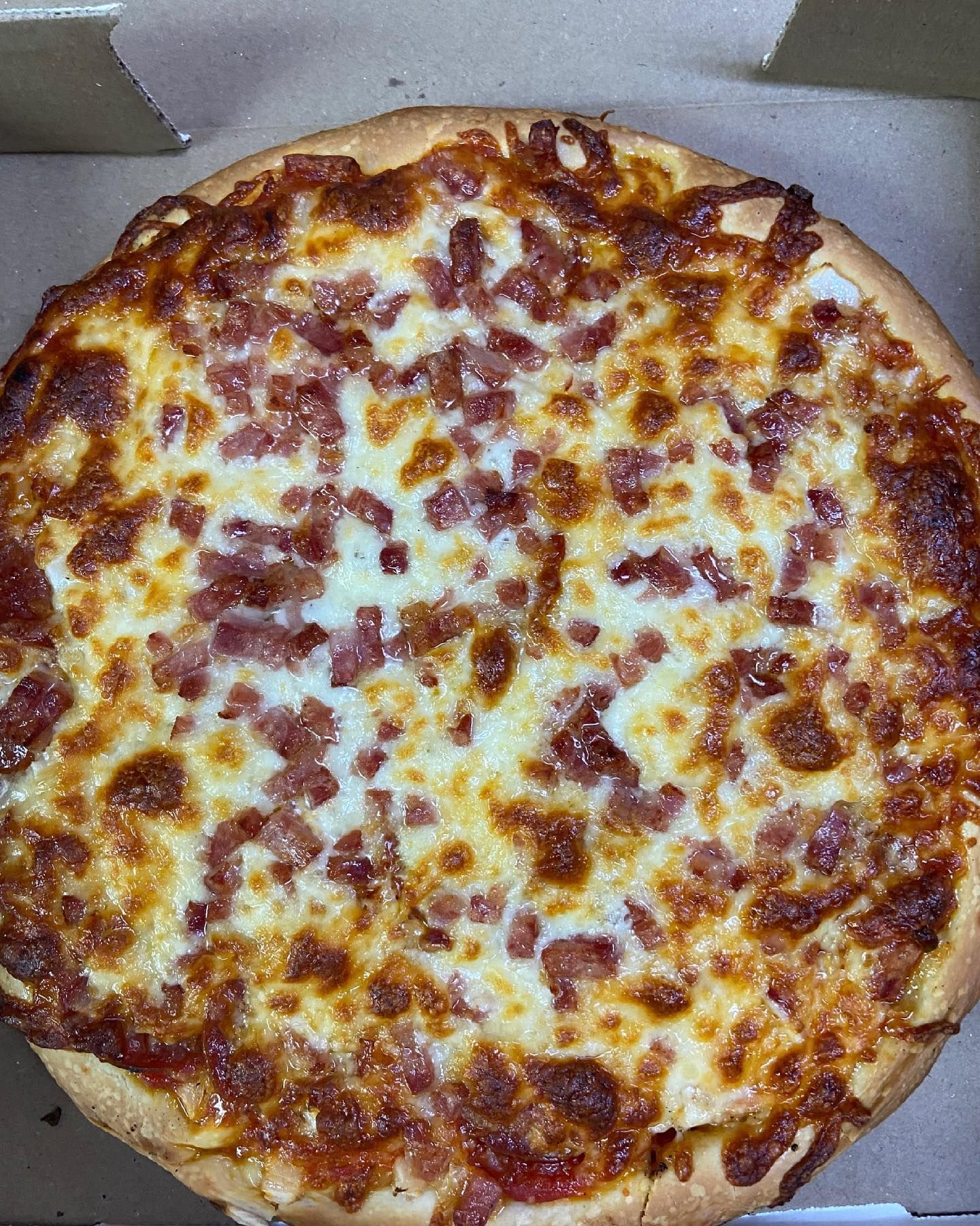 A pizza with a lot of cheese and bacon on it is in a box.