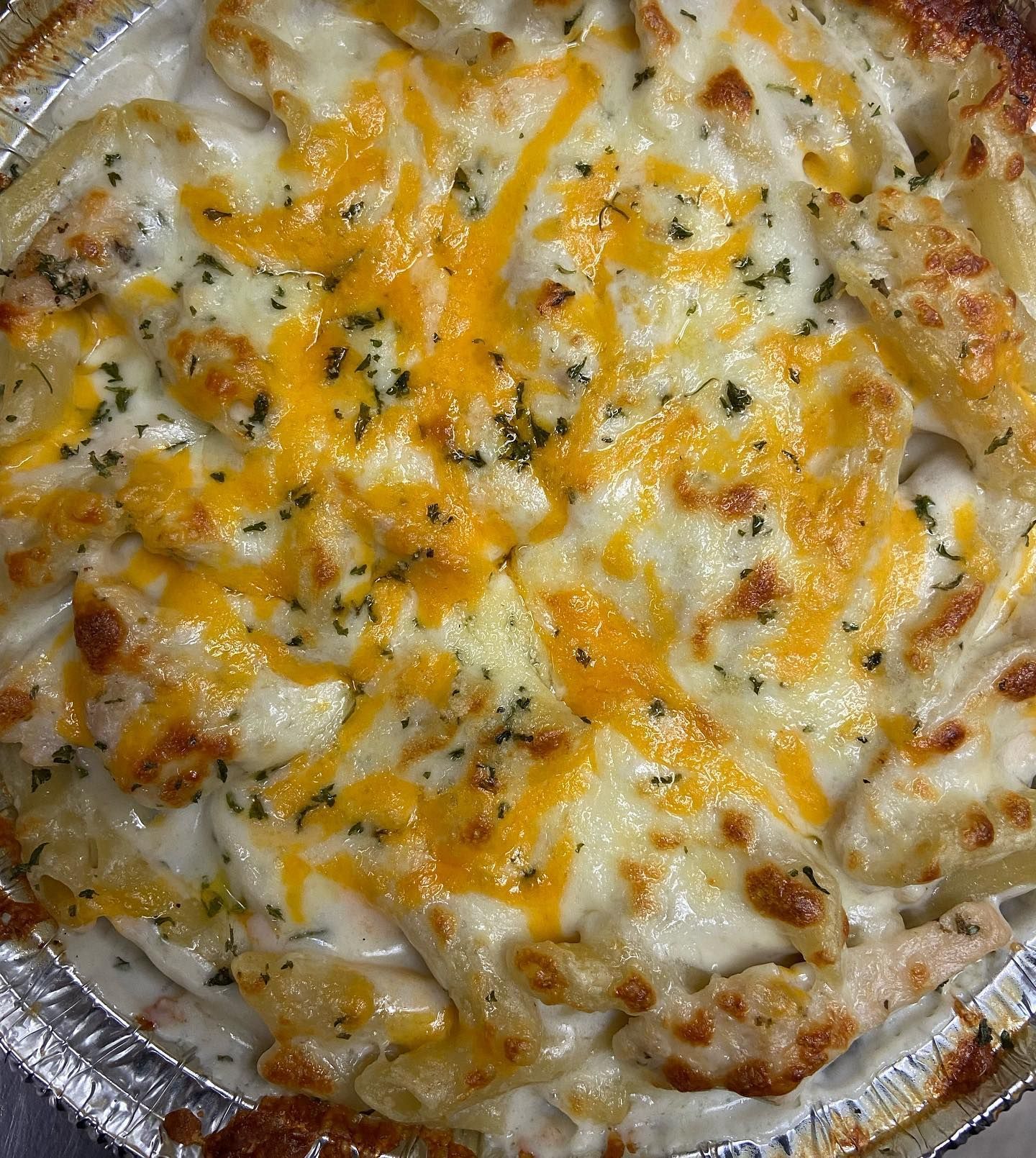 A close up of a macaroni and cheese pizza in a tin foil pan.