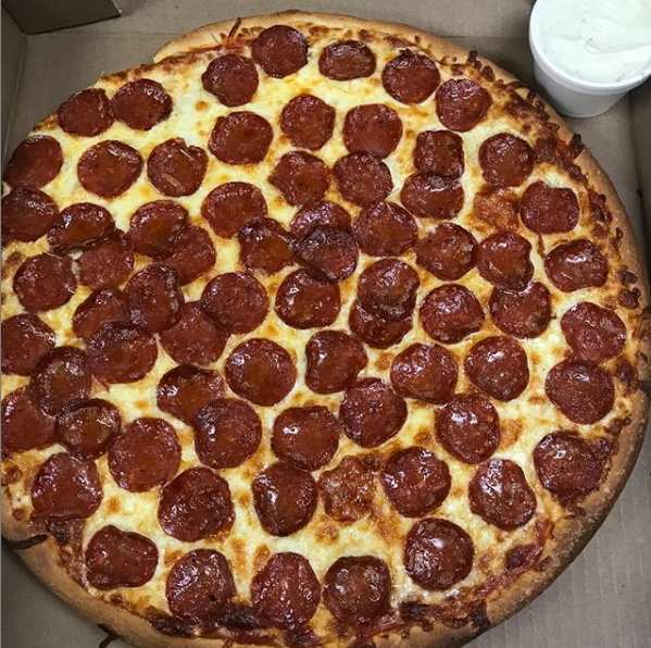 A pizza is sitting on a wooden table and has a lot of cheese on it