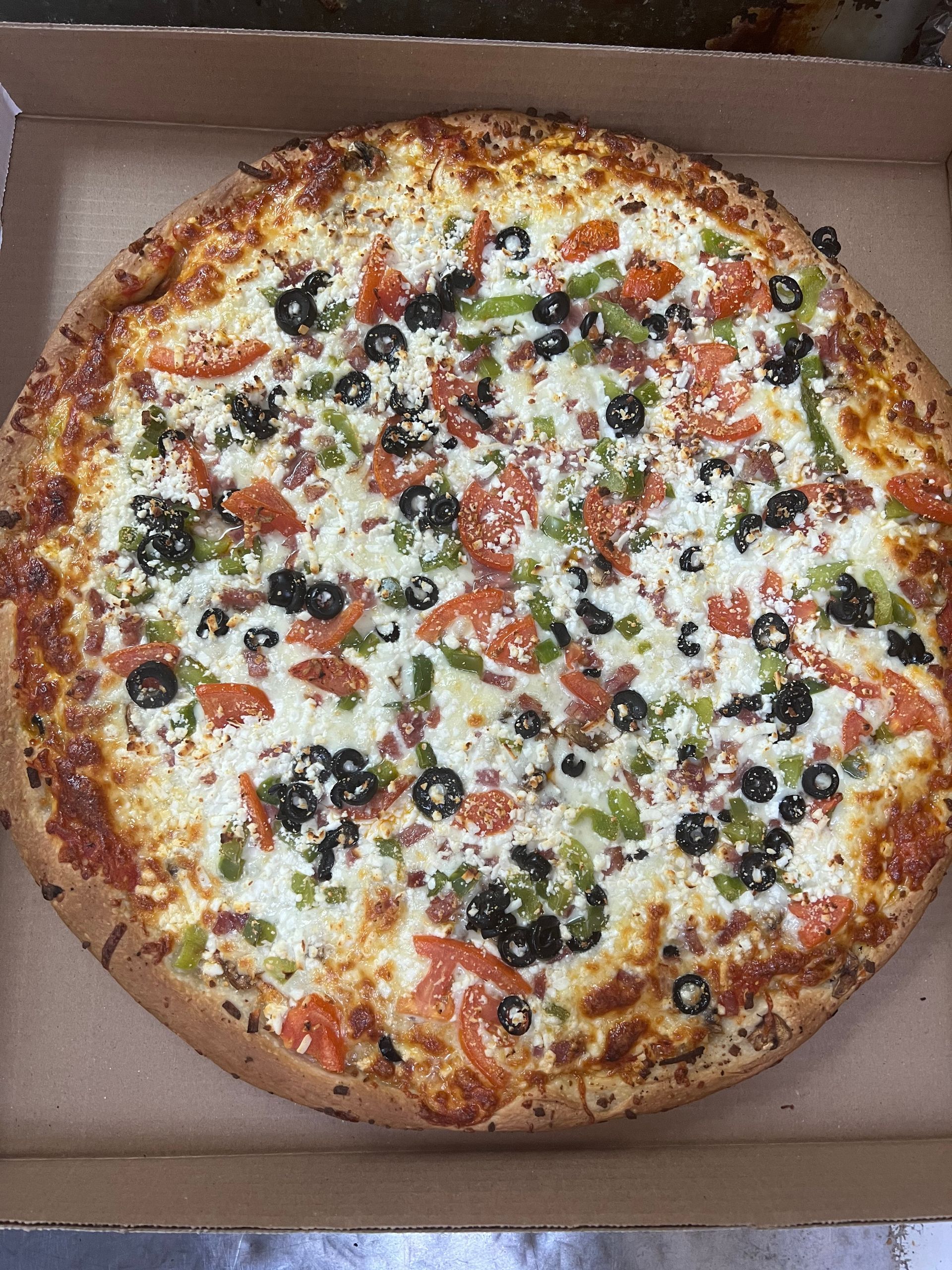 A pizza with tomatoes , peppers , olives and cheese is in a box.