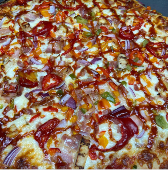 A pizza with chicken , bacon and onions on a wooden cutting board.