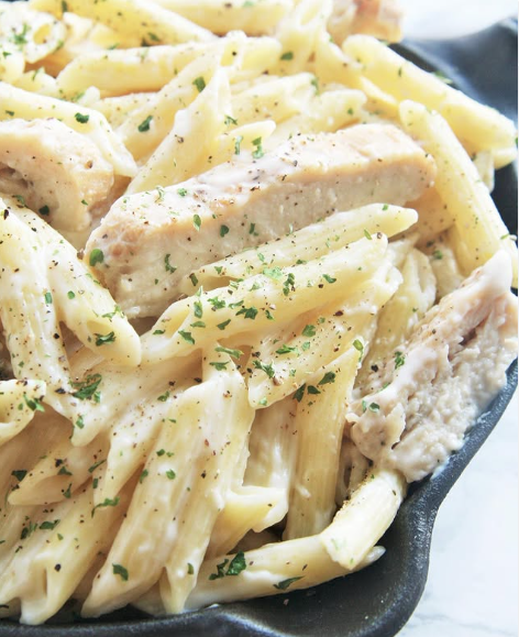 A slice of lasagna on a white plate with basil on top.