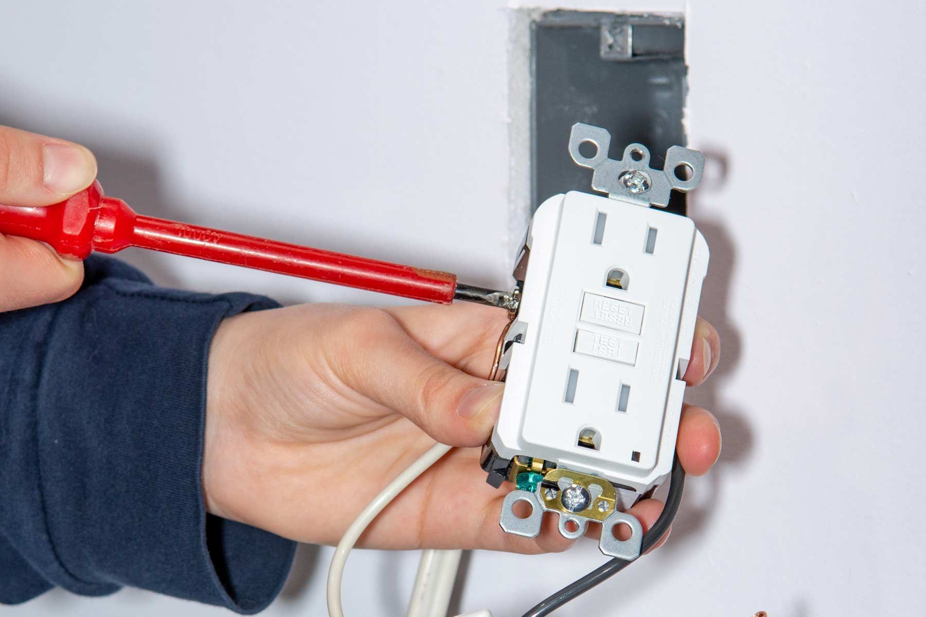 A person is fixing an electrical outlet with a screwdriver.