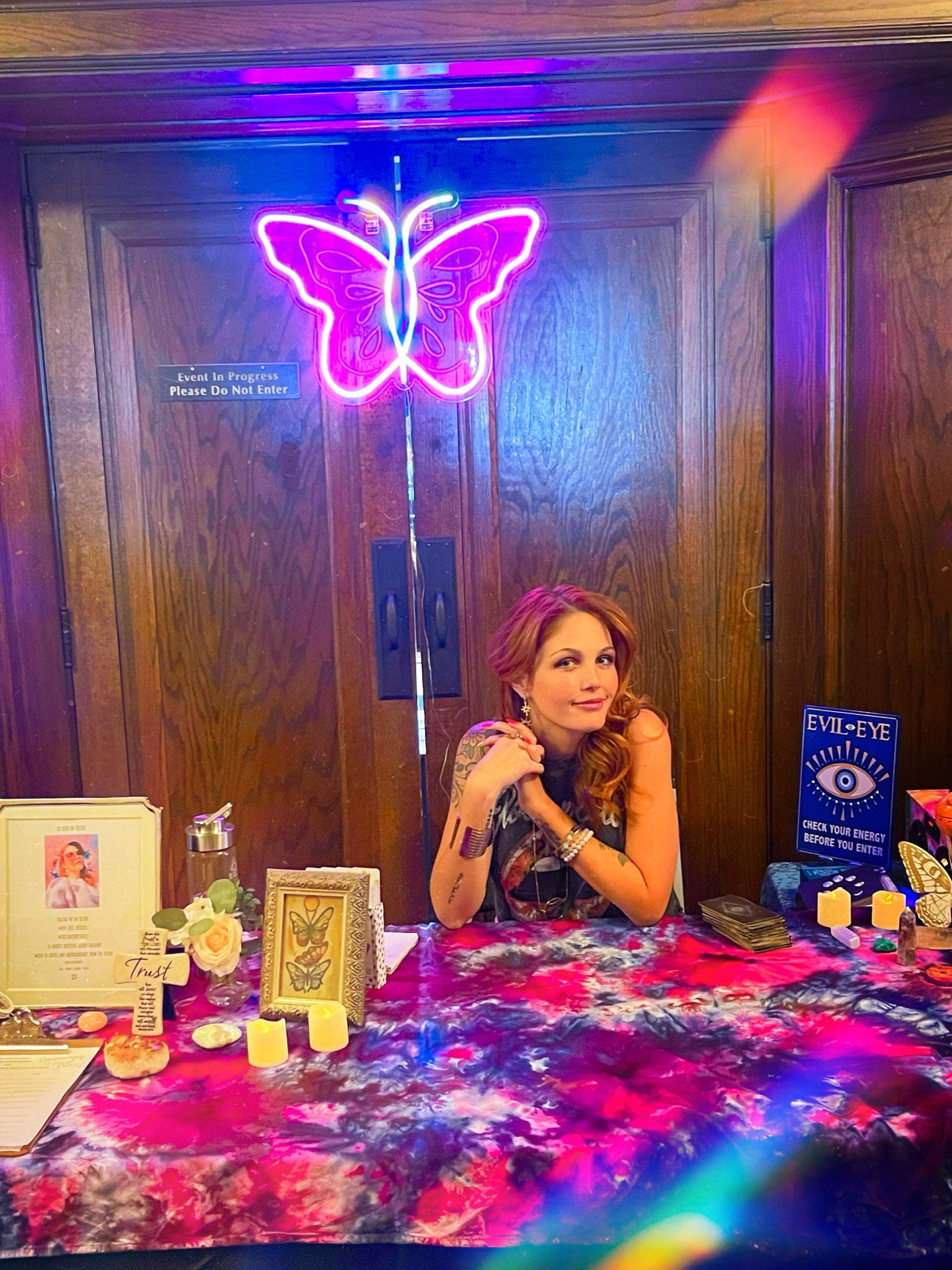 A woman is sitting at a table under a neon butterfly sign.