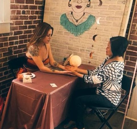 A woman is sitting at a table with a painting of frida kahlo on the wall.