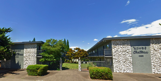 Two-story apartment buildings with a stone facade, Royat Chateau, under a blue sky.