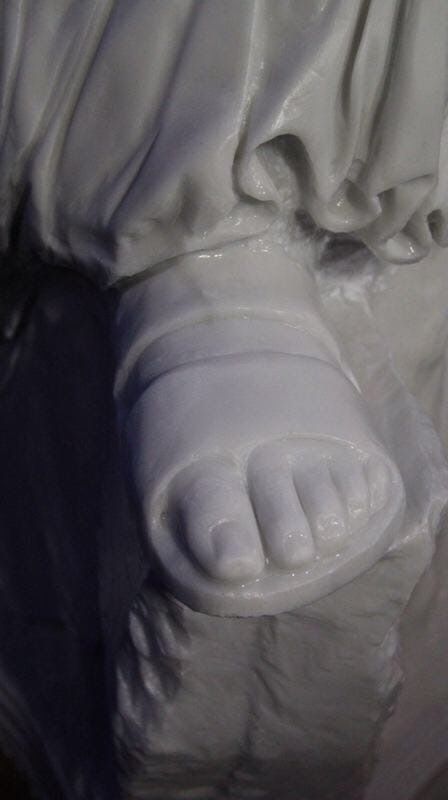 Primer plano de un pie de mármol blanco que lleva una sandalia, parte de una escultura.
