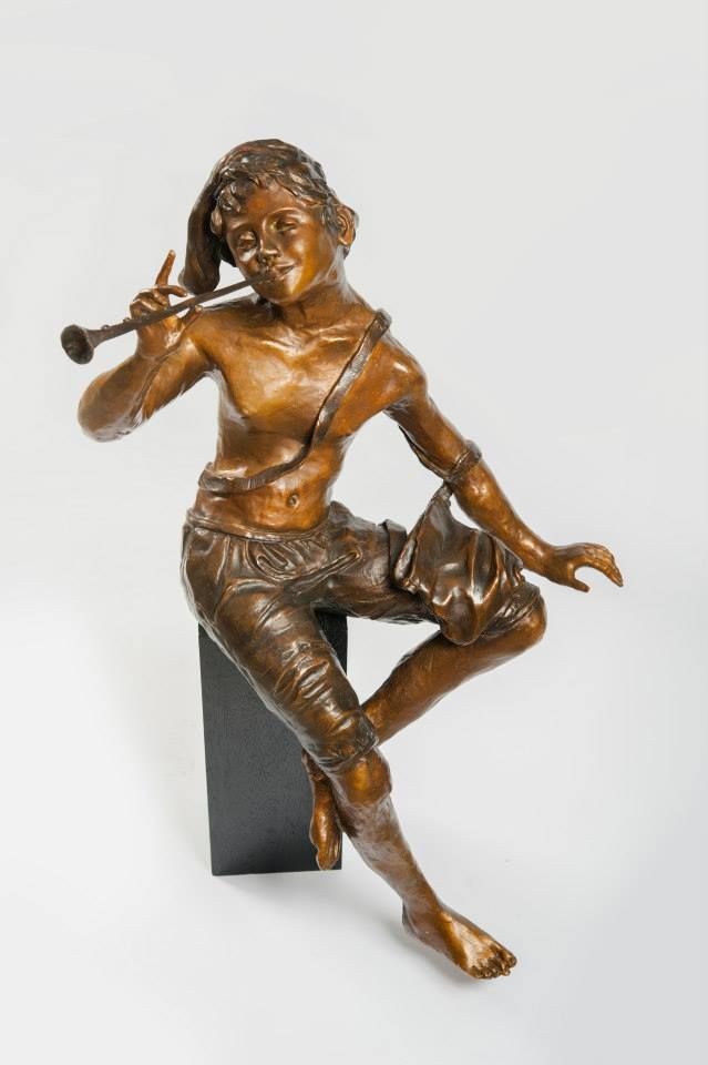 Escultura de bronce de un niño tocando la flauta mientras está sentado, con expresión alegre.
