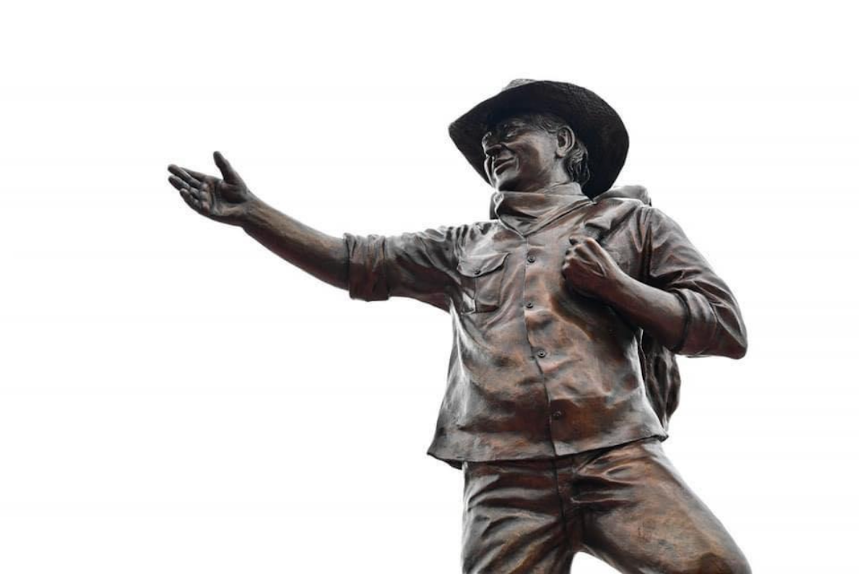 Estatua de bronce de un hombre con sombrero, mochila y ropa informal, con el brazo extendido y señalando.