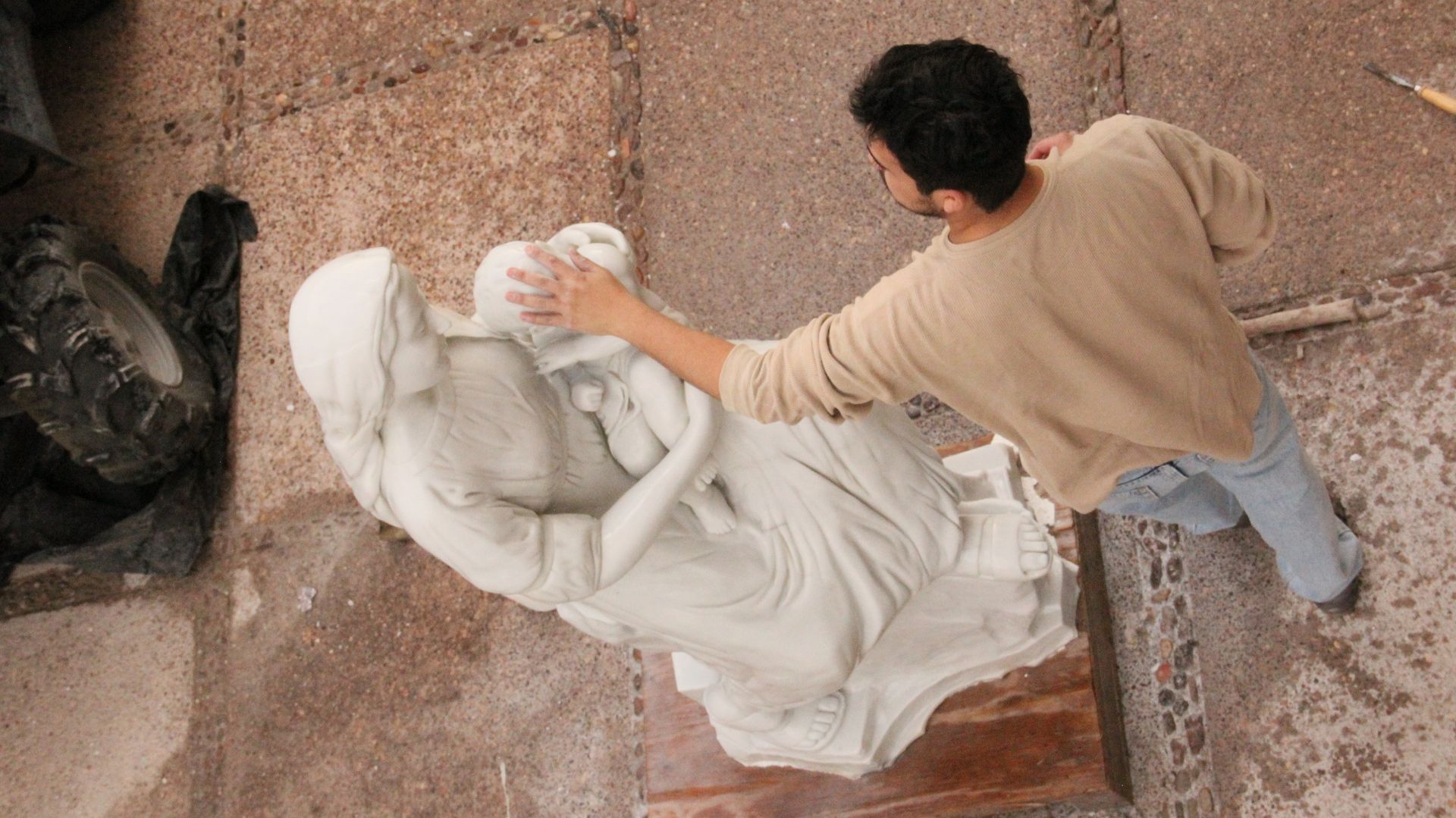 Escultor trabajando en una estatua blanca en un taller, vista desde arriba.