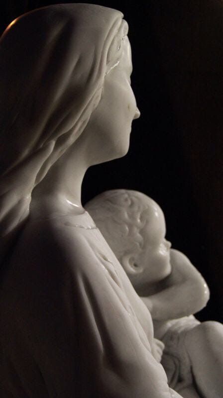 Estatua de mármol de la Virgen con el Niño, blanca sobre fondo negro.