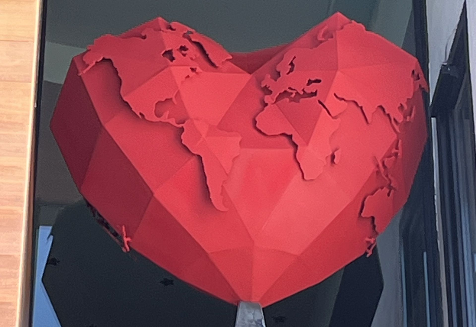 Escultura roja en forma de corazón del mapa del mundo exhibida en una ventana.