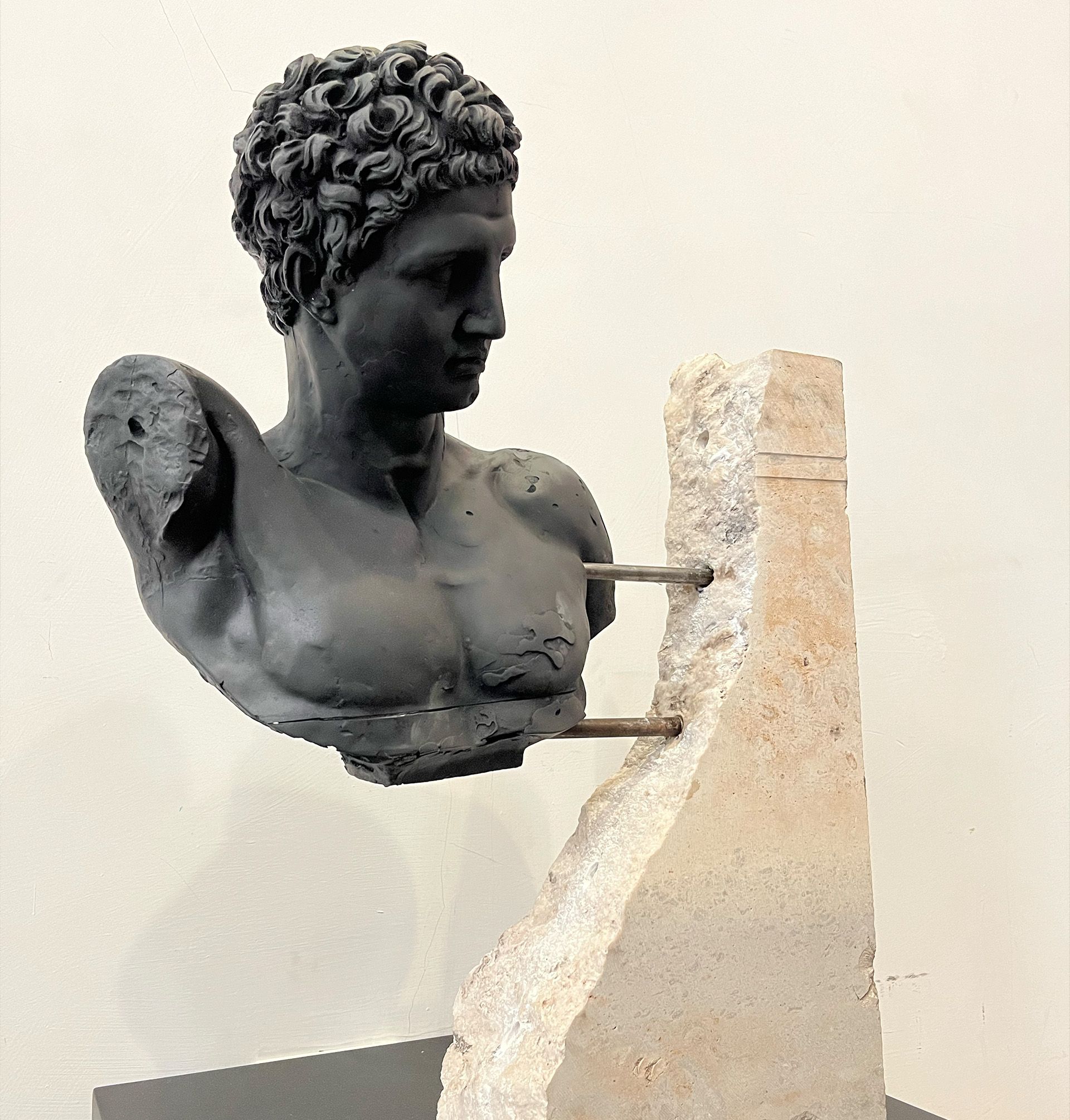 Busto oscuro de un hombre mirando hacia la derecha, montado sobre un bloque de piedra con varillas de metal.