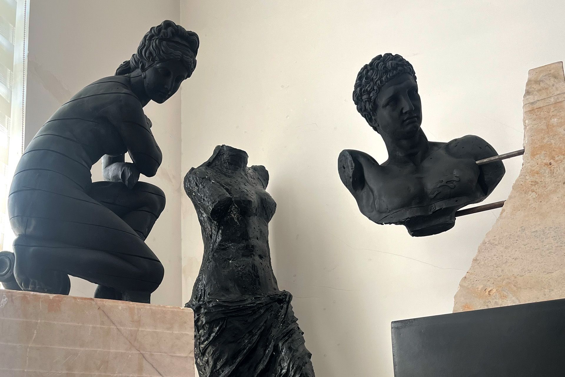 Esculturas negras de figuras humanas en exhibición: una mujer arrodillada, un torso y un busto.