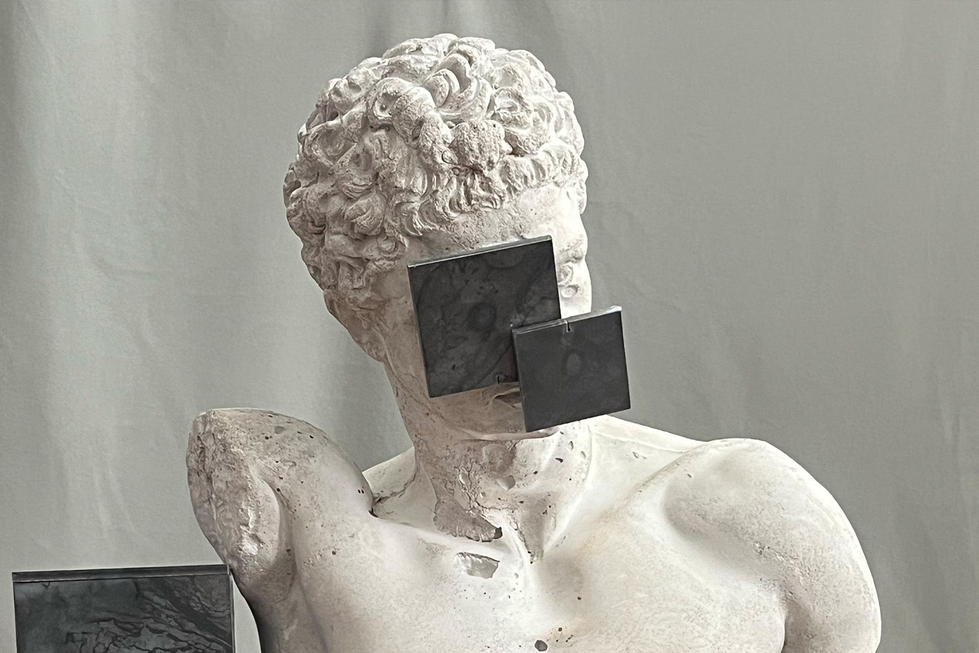 Busto de estatua de concreto con dos cuadrados negros de acero cubriendo el rostro.