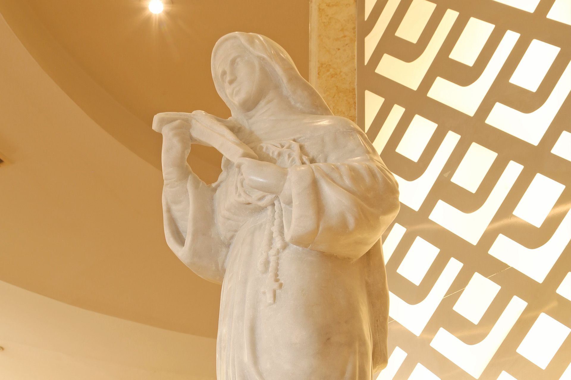 Estatua de mármol blanco de Santa Rita de Casia sosteniendo un crucifijo y un rosario.