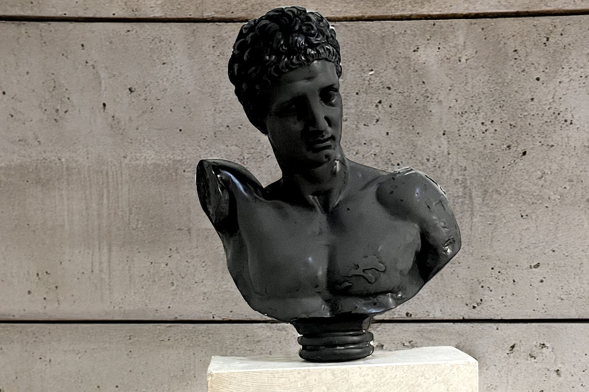 Busto negro de gaucho de un hombre sobre un pedestal contra una pared de hormigón gris; tiene una expresión estoica y cabello rizado.