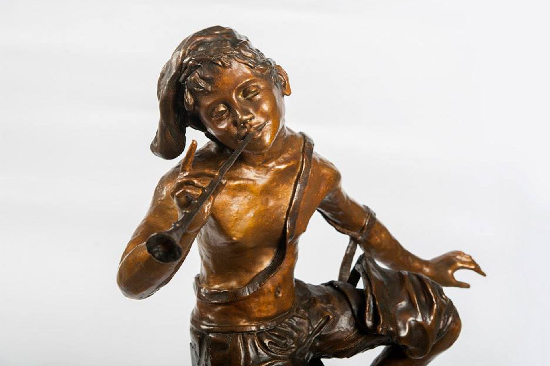 Escultura de bronce de un niño tocando la trompeta, con una bolsa colgada del hombro.