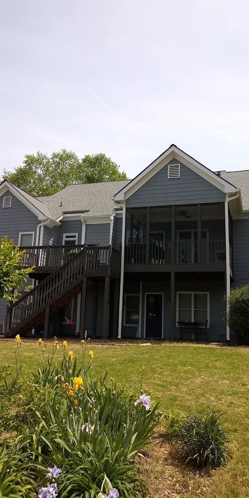 A large house with a large deck is sitting on top of a lush green lawn