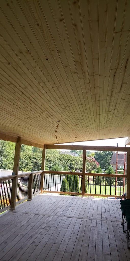 A large wooden deck with a wooden ceiling and railing.