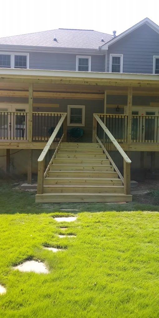 A large wooden deck with stairs leading up to it is in the backyard of a house