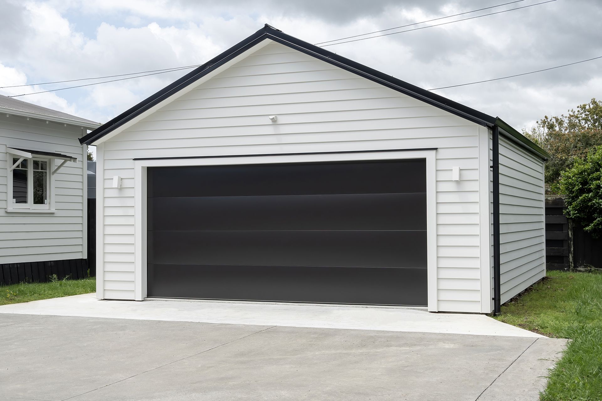 A white garage with a black door is next to a house.