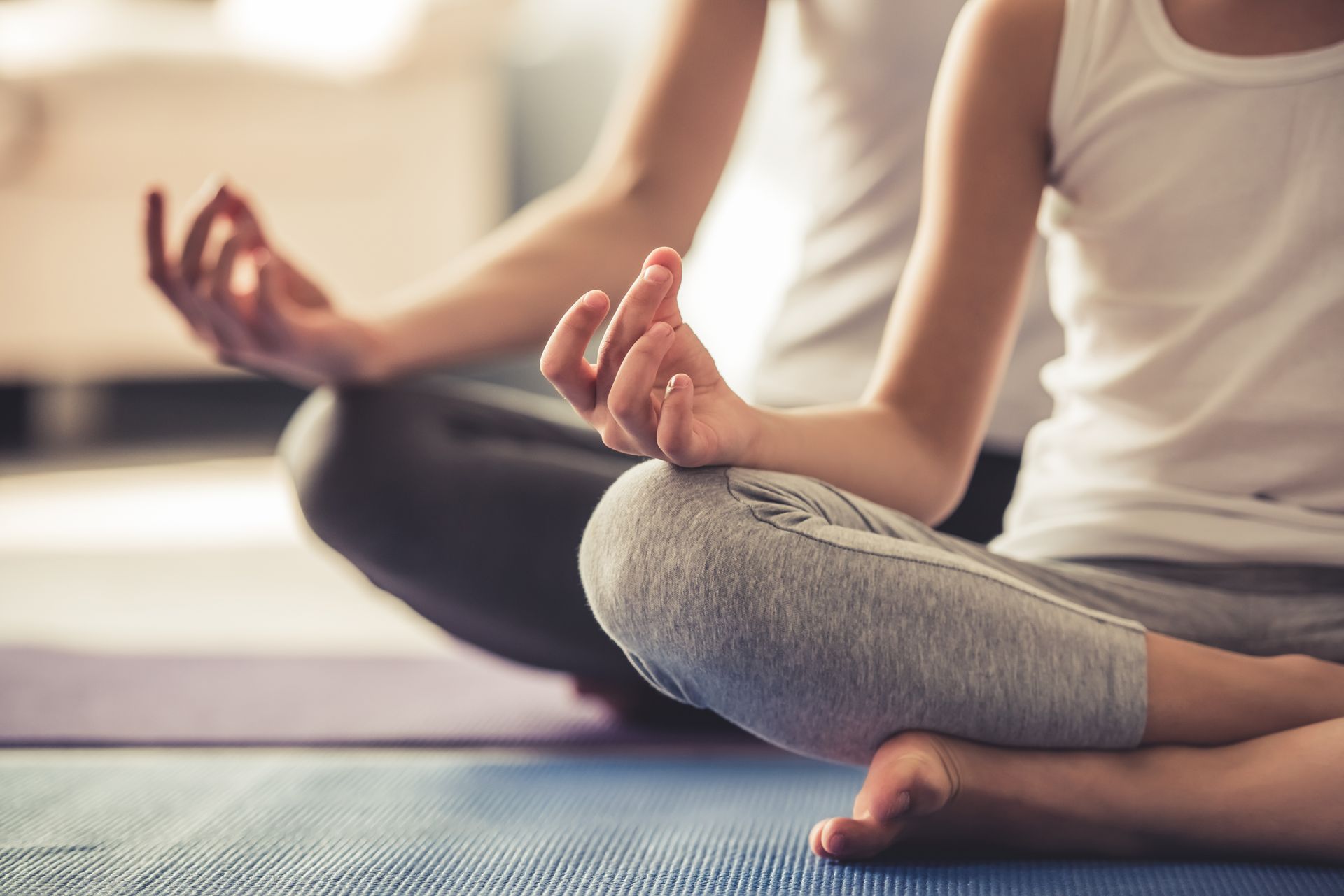 A woman and a child are sitting in a lotus position on a yoga mat.