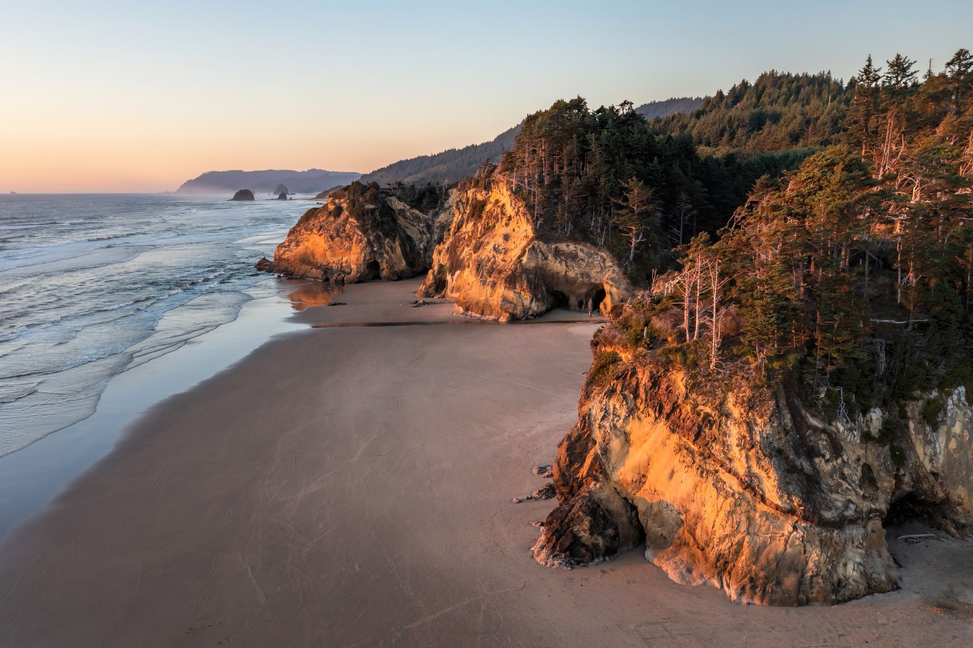 An aerial view of a beach with cliffs and trees in the background.