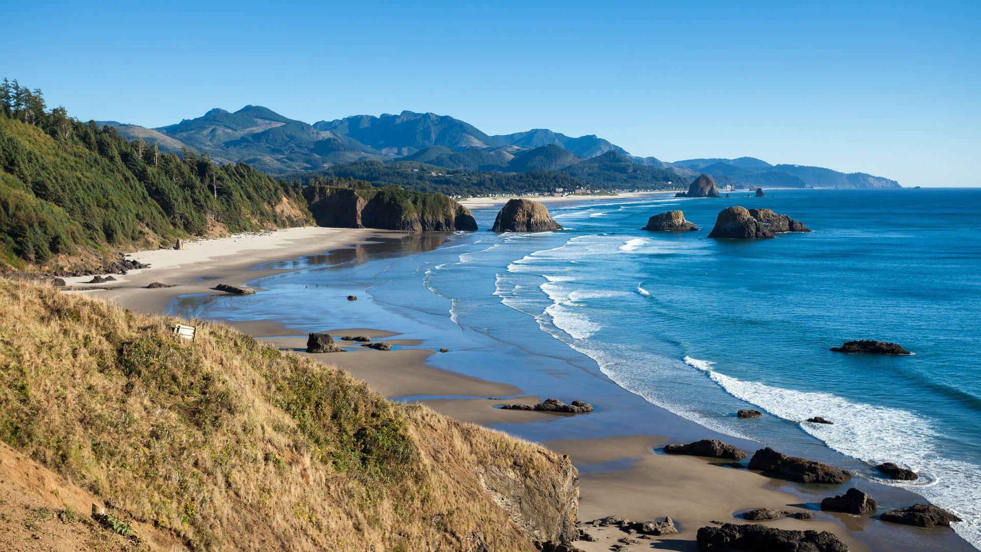 A beach with mountains in the background and waves crashing on the shore.