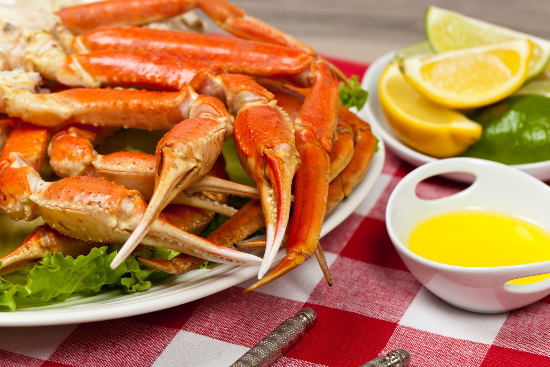 A plate of crab legs on a checkered google table cloth next to a bowl of butter.