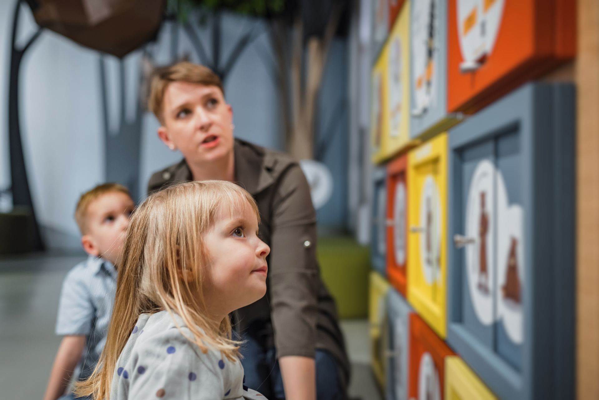 Woman and two children look at colorful, interactive wall display.