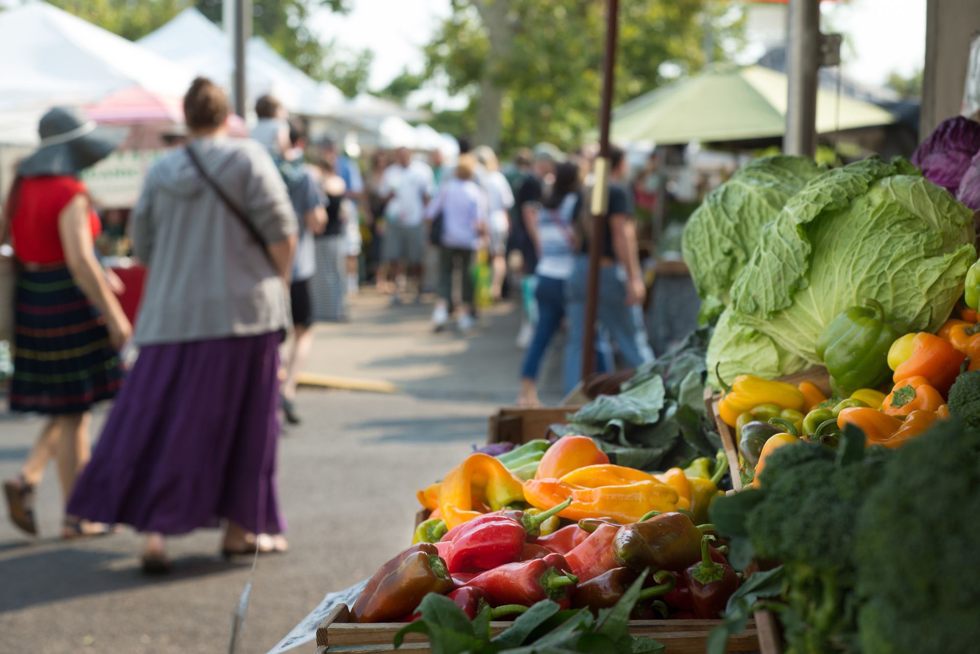 Produce display with shoppers at a farmers market.
