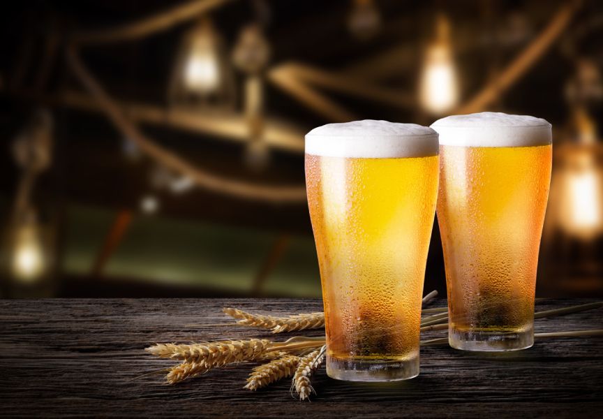 Two glasses of beer and wheat ears on a wooden table.