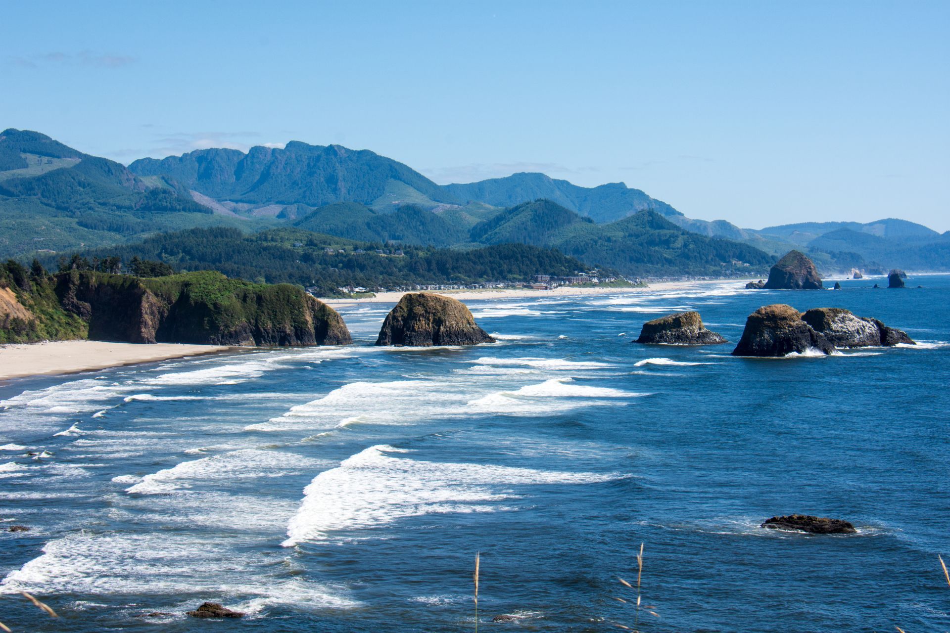 A view of a beach with mountains in the background and waves crashing on the shore.