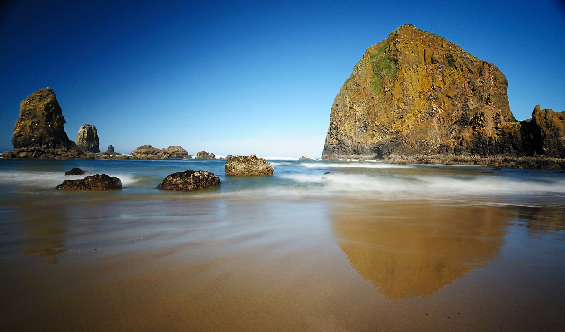 There is a large rock in the middle of the ocean on the beach.