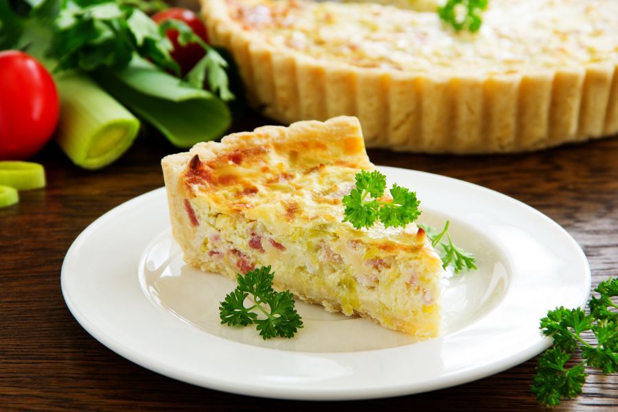 A slice of quiche is on a white plate.