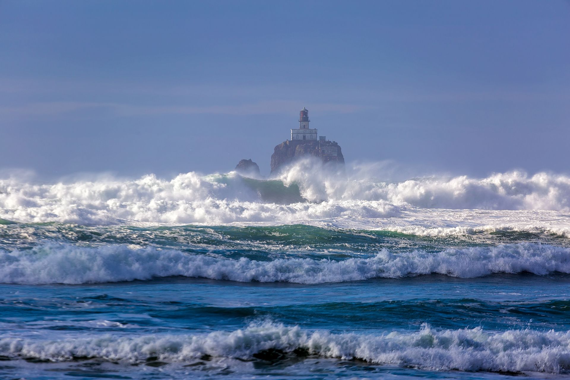 A large rock in the middle of the ocean with waves crashing against it.