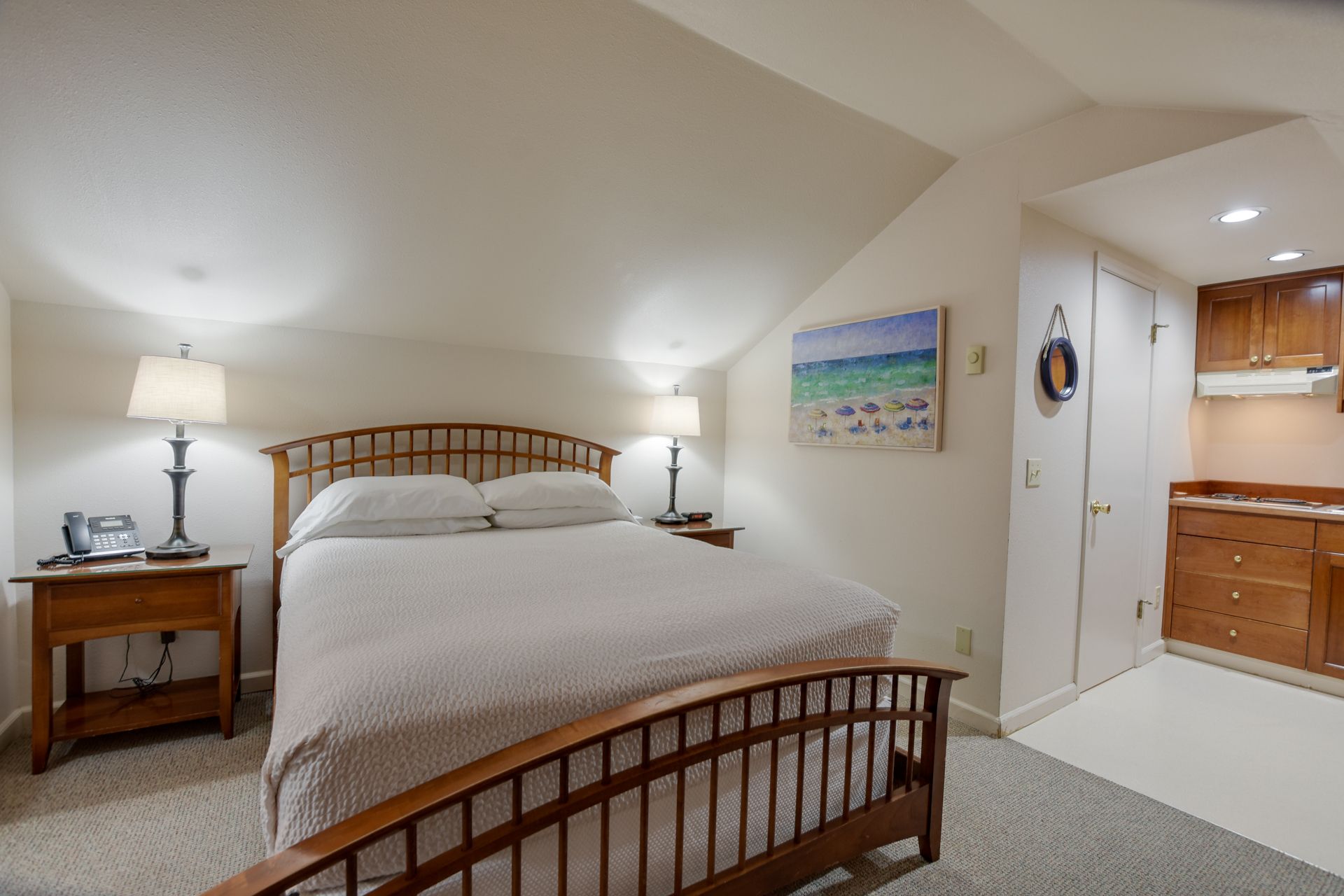 A bedroom with a king size bed and a kitchen in the background.