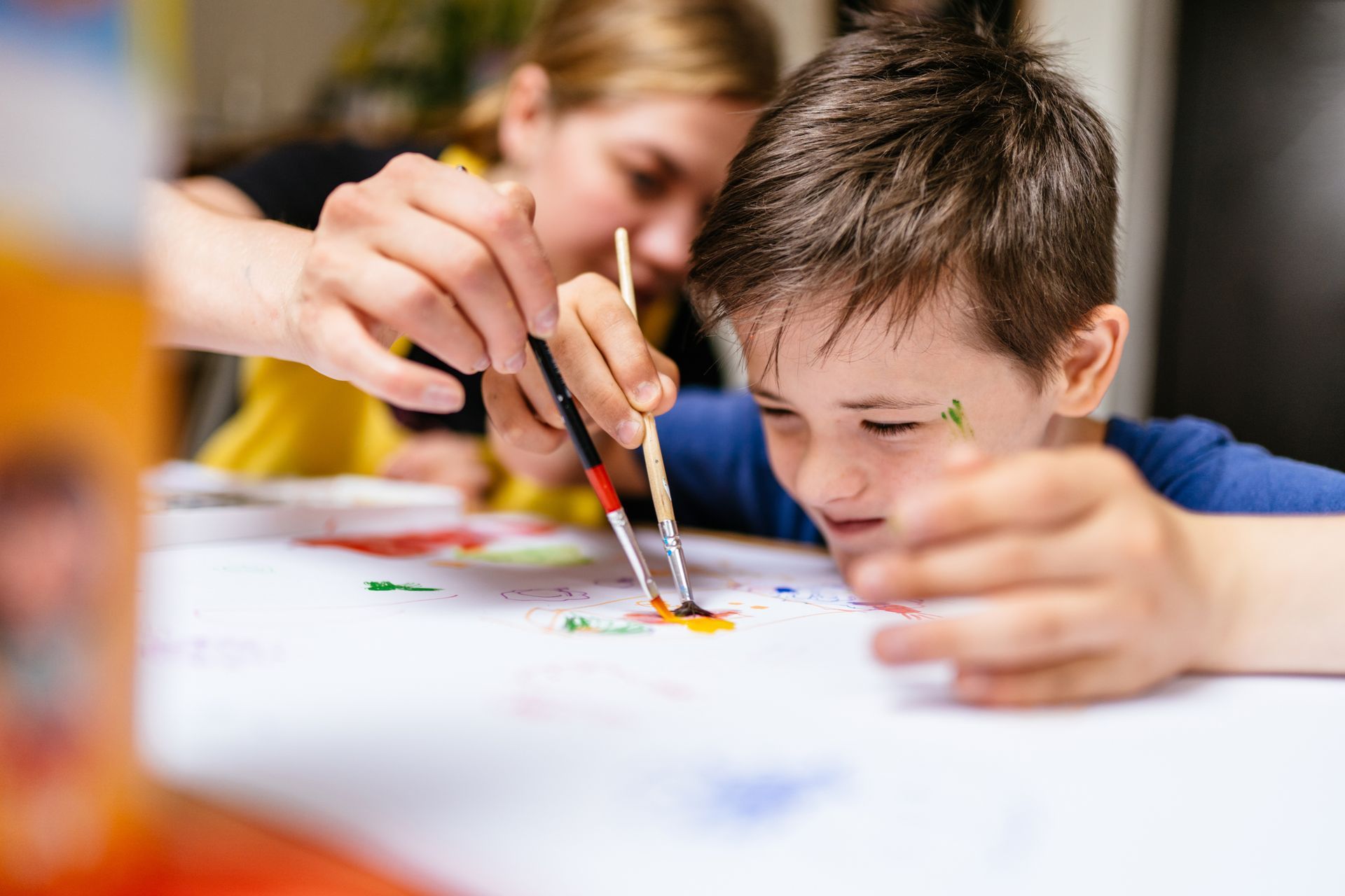 A young boy is sitting at a table painting with a brush.