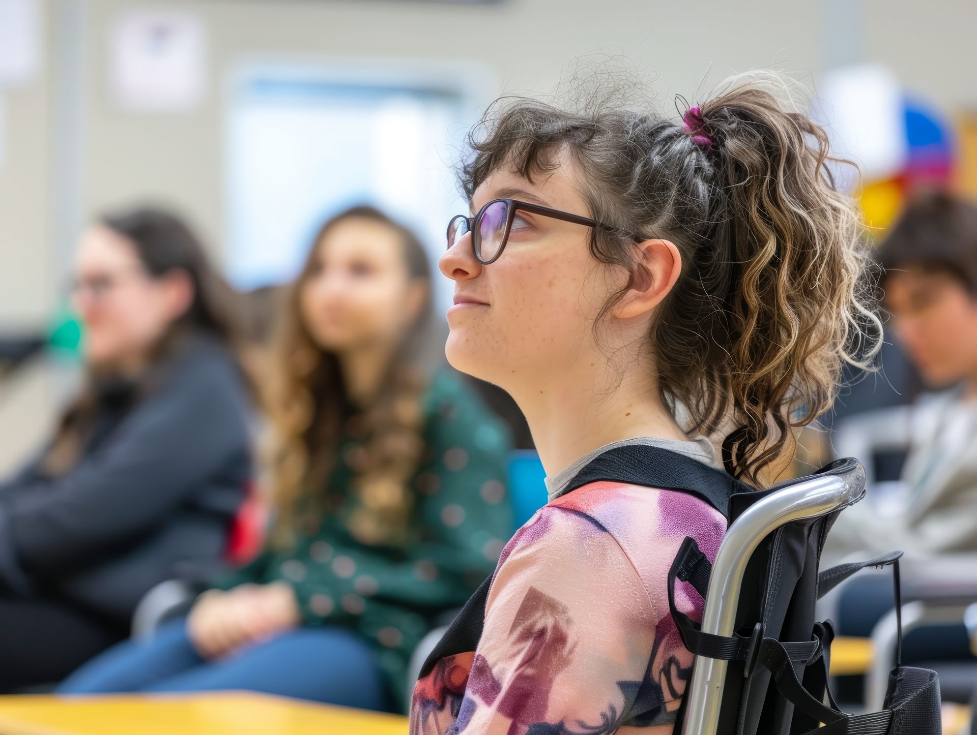 A woman in a wheelchair is sitting in a classroom with other students.