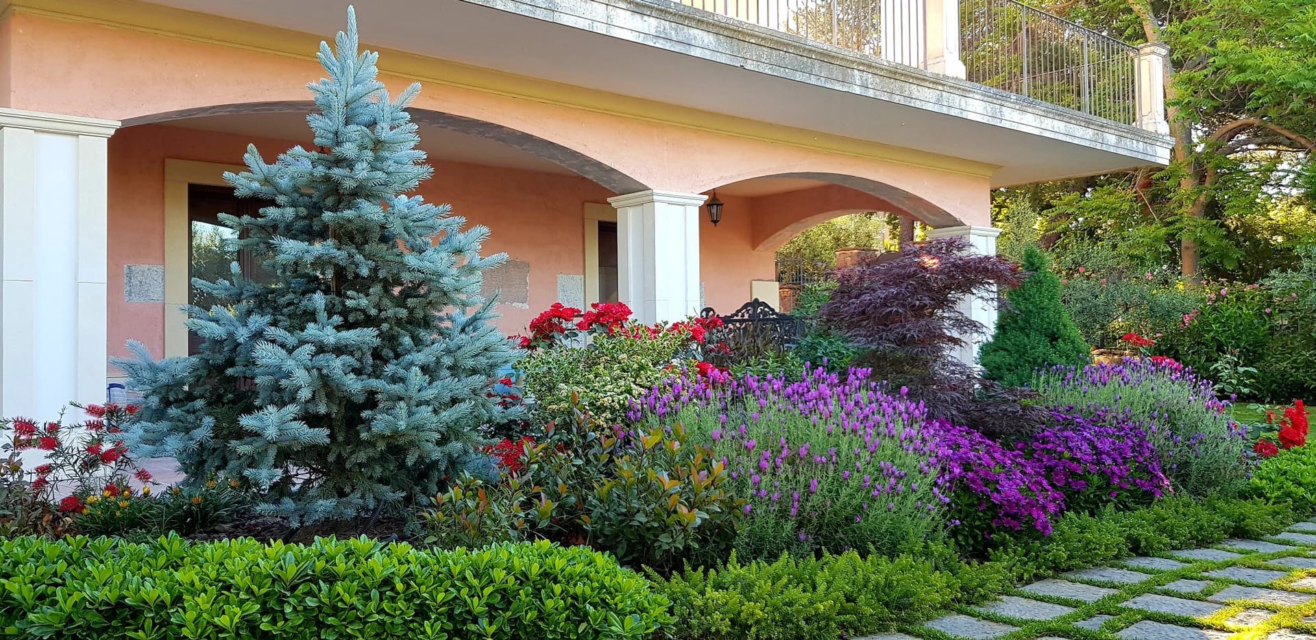 Esterno di un edificio con facciata rosa, portico ad arco e un giardino colorato con un sentiero in pietra.