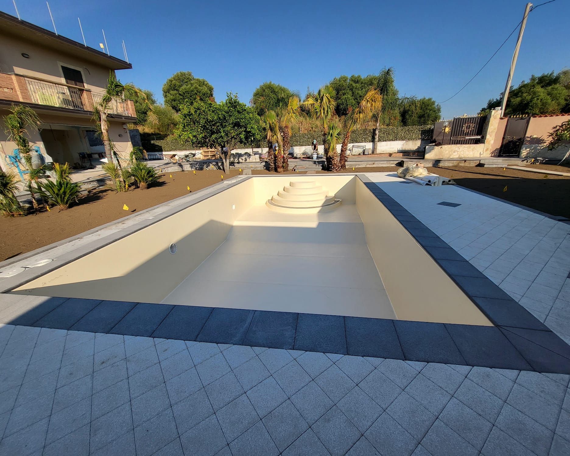 Piscina rettangolare vuota con interno color cuoio, circondata da un bordo grigio scuro e da una pavimentazione grigio chiaro.