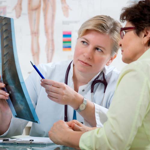 Doctor shows the problem areas on a X-ray to patient and explains the cause of her pain.