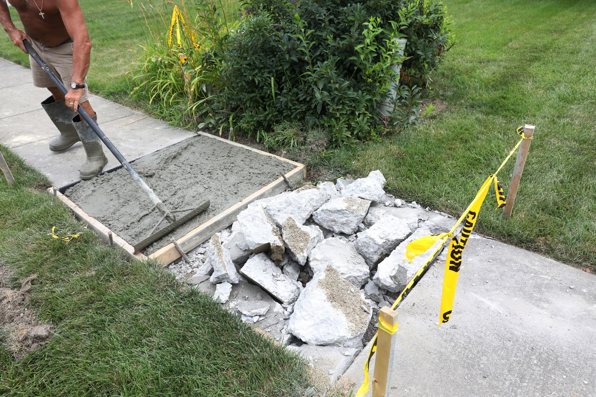 A man is spreading concrete on a sidewalk with a broom.