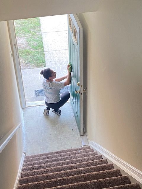 A woman is cleaning a door in a hallway next to stairs.