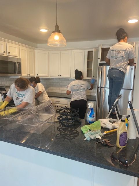 A group of people are cleaning a kitchen with white cabinets and stainless steel appliances.