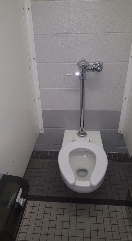 A toilet is sitting in a public restroom next to a trash can.